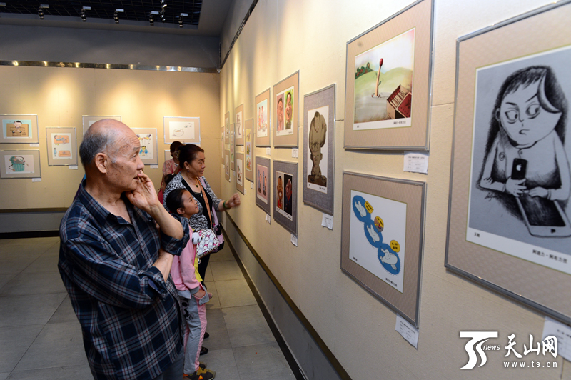 “新疆新闻漫画作品展”在乌鲁木齐文化馆开展,市民参观展览。